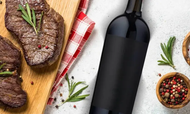 Idealne jakie wino do steka? Soczyste steki na desce, butelka czerwonego wina i przyprawy.