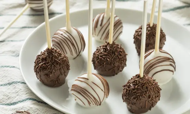 Pyszne cake pops przepis na talerzu: czekoladowe z posypką i białe z polewą.