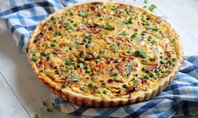 Pyszna tarta z porem i boczkiem, udekorowana groszkiem i ziołami, na niebiesko-białej kratce.