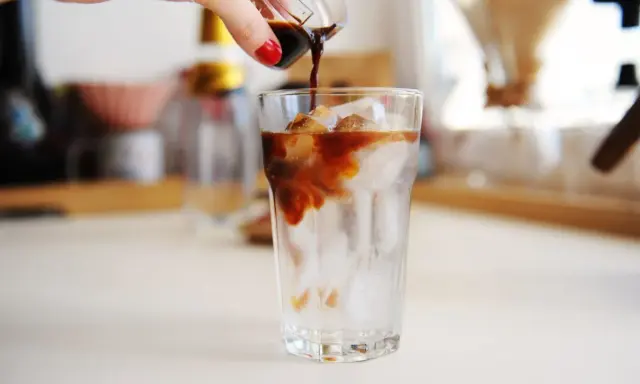 Ręka wylewa espresso na lód w szklance. Idealny napój na upalne dni - tonic espresso.