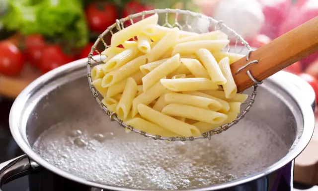 Penne makaron w cedzaku nad garnkiem z wrzącą wodą. Czas, ile się gotuje makaron, zależy od jego rodzaju.