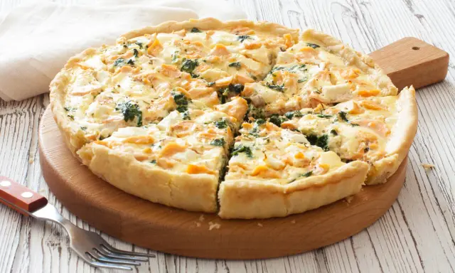 Pyszna tarta z łososiem, szpinakiem i serem feta, pokrojona na kawałki, czeka na talerzu.