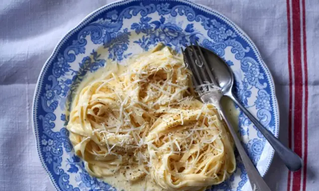 Pyszny makaron alfredo przepis na talerzu z widelcem i łyżką, posypany startym parmezanem.