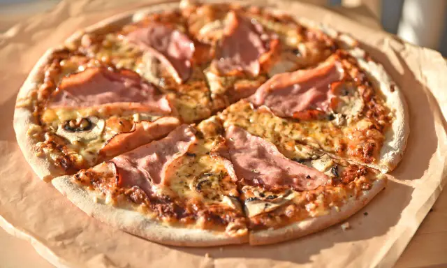 Pizza z szynką i pieczarkami do pizzy, pachnąca i apetyczna, gotowa do podania.