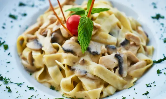 Pyszny makaron tagliatelle z kremowym sosem pieczarkowym, udekorowany pomidorkiem koktajlowym i listkiem mięty.