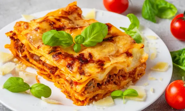 Pyszna, domowa lasagne jak z pieca, z warstwami makaronu, mięsa i sera, ozdobiona świeżą bazylią i parmezanem.