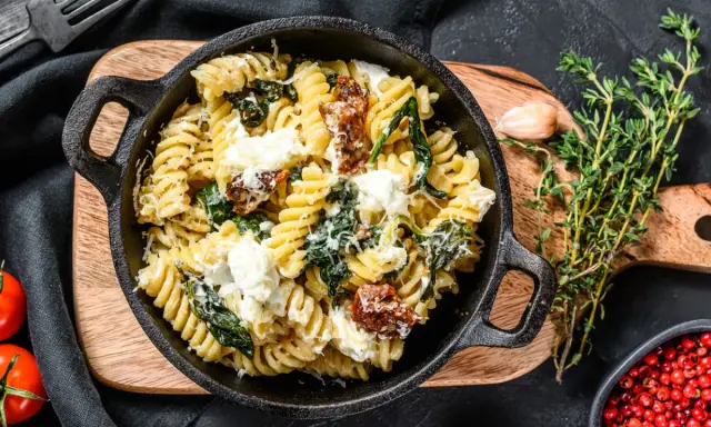 Pyszne fusilli ze szpinakiem i suszonymi pomidorami, posypane parmezanem i kawałkami sera feta.