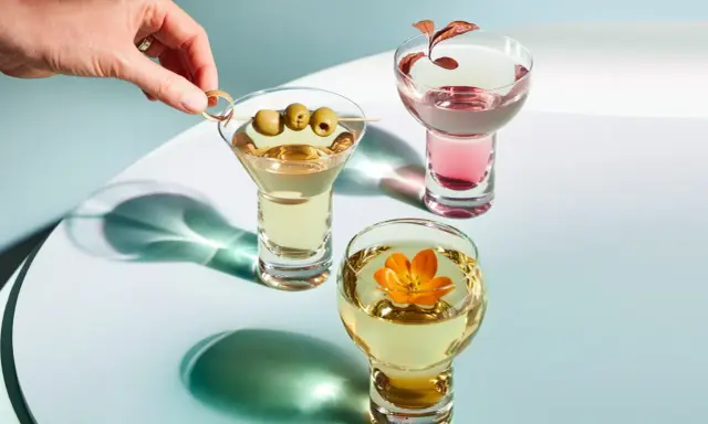 Eleganckie drinki z wódką: martini z oliwkami, różowy koktajl i złoty napój z kwiatem.