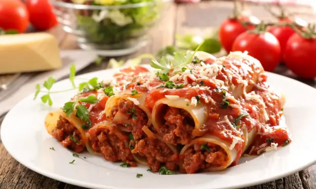 Pyszne cannelloni z mięsem mielonym, polane sosem pomidorowym i posypane parmezanem, na talerzu z pomidorami i sałatką.