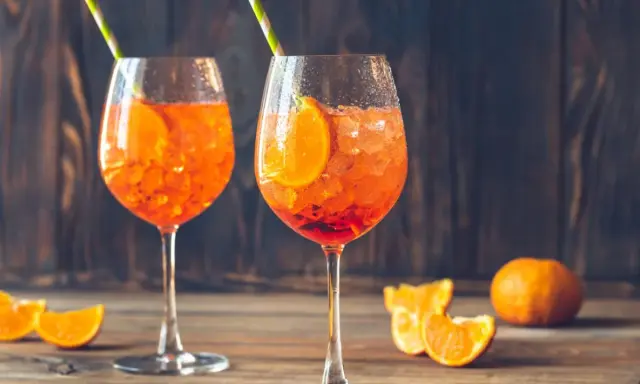 Dwa orzeźwiające drinki z aperolem i sokiem pomarańczowym, ozdobione plasterkami pomarańczy i podane z kolorowymi słomkami. Idealne na letnie popołudnie.