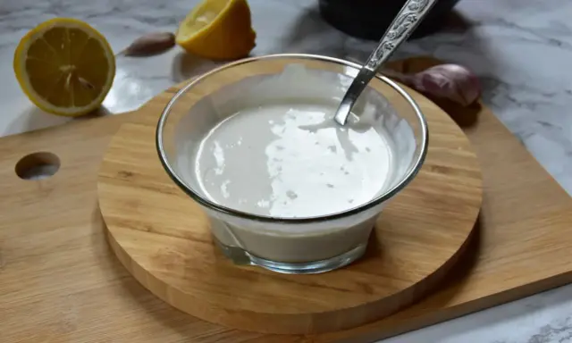 Kremowy sos aioli w szklanej miseczce, obok cytryny i czosnku. Idealny dodatek do dań.