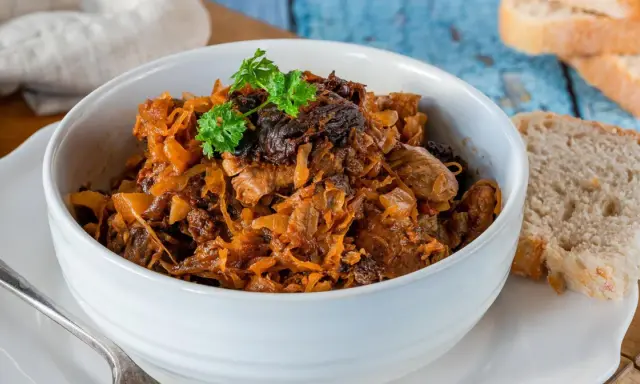 Pyszny bigos w białej misce, z gałązką natki pietruszki. Obok kromki chleba. Idealny na zimowe wieczory.