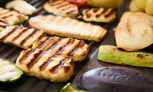 Grillowany ser halloumi z paskami od rusztu, obok cukinia, bakłażan i inne warzywa.