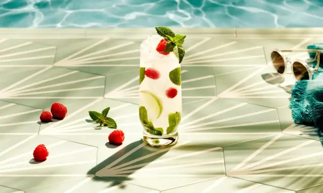 Orzeźwiający drink z malinami i miętą, idealny do Bacardi malinowego. Obok leżą maliny, a w tle widać basen i okulary przeciwsłoneczne.