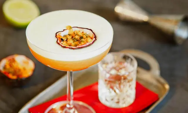 Pyszny drink Pornstar Martini z pianką i owocem marakui, obok kieliszek z drinkiem i połówka limonki.