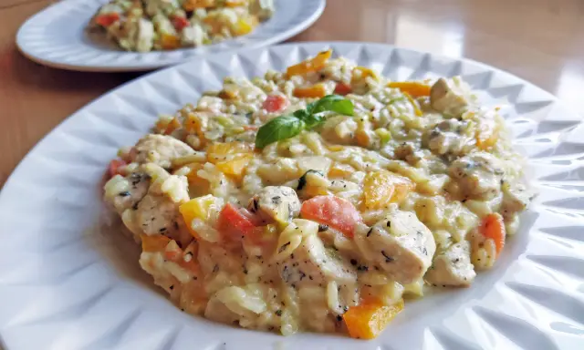 Pyszne risotto z kurczakiem i kolorowymi warzywami, udekorowane listkiem bazylii. Idealne na obiad.