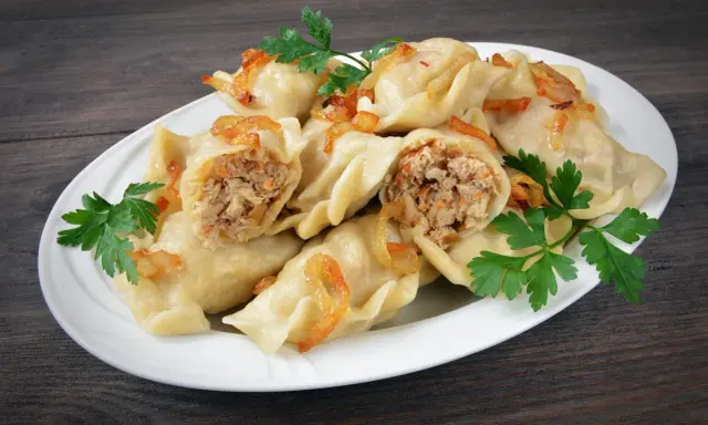 Pyszne pierogi z mięsem i kapustą, okraszone skwarkami i udekorowane natką pietruszki, na białym talerzu.