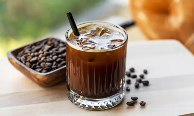Orzeźwiający cold brew z lodem i słomką, obok miseczka z ziarnami kawy. Idealny na gorący dzień.