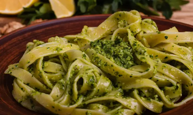 Pappardelle z aromatycznym makaronem z pesto, podane na glinianym talerzu. W tle cytryny i rukola.