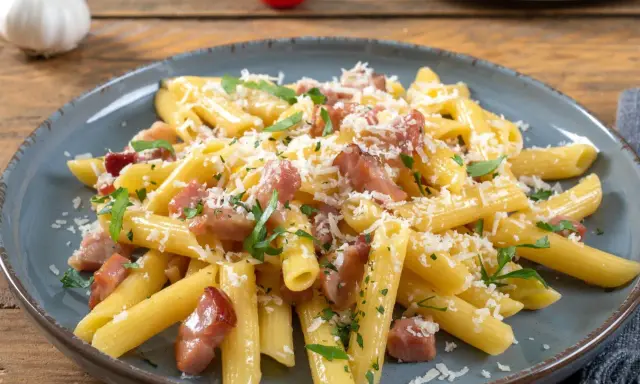 Penne rigate z chrupiącym boczkiem, posypane parmezanem i natką pietruszki. Pyszne makaron z boczkiem na talerzu.