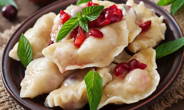 Pyszne, domowe ciasto na pierogi z wiśniami i miętą, podane na glinianym talerzu.