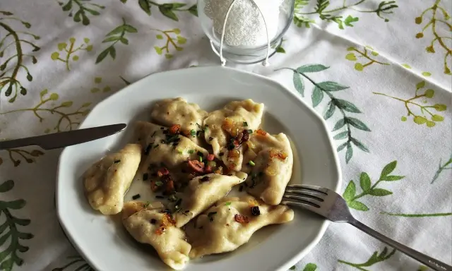 Pyszne pierogi ruskie z cebulką i boczkiem, gotowe do jedzenia. Obok widelec i nóż.