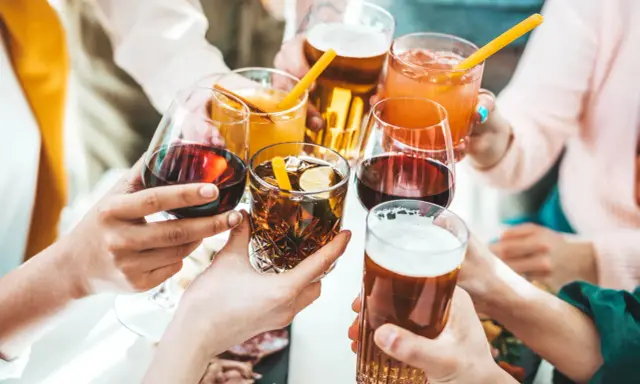 Ręce wznoszą kieliszki z winem, drinkami i piwem, celebrując wspólne chwile.