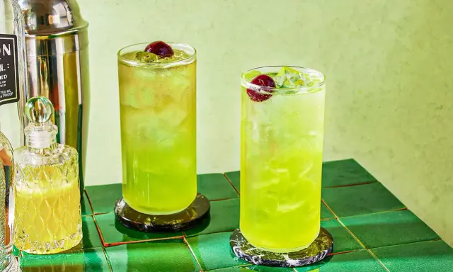 Dwa orzeźwiające drinki Tokyo Ice Tea z wiśniami i lodem, obok shakera i buteleczki z likierem.