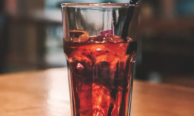 Szklanka z lodem i ciemnym napojem, idealne proporcje whisky z colą. Czarna słomka zanurzona w napoju.