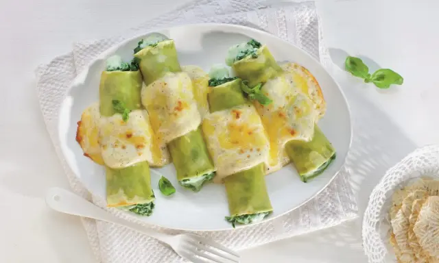 Zielone cannelloni ze szpinakiem, polane kremowym sosem i zapieczone z serem. Pyszne danie gotowe do podania.