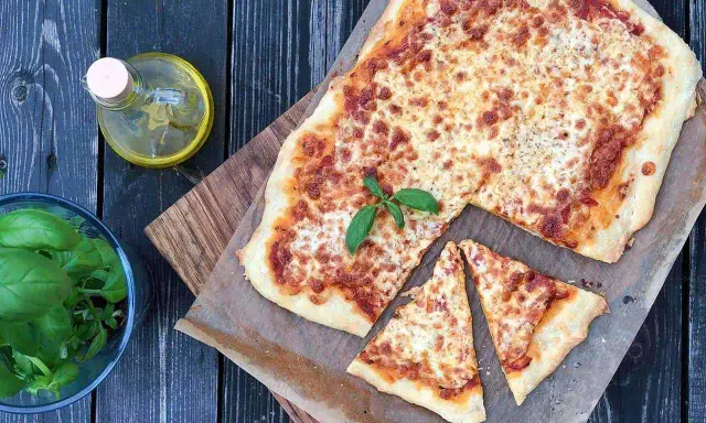 Pyszna pizza margherita z roztopionym serem i świeżą bazylią, obok butelka oliwy i miseczka ziół.