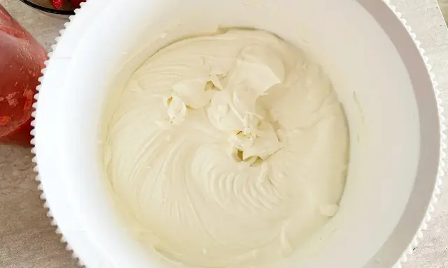 Gładki, puszysty krem z mascarpone w białej misie, gotowy do deseru. Obok miski widać miseczkę z truskawkami.