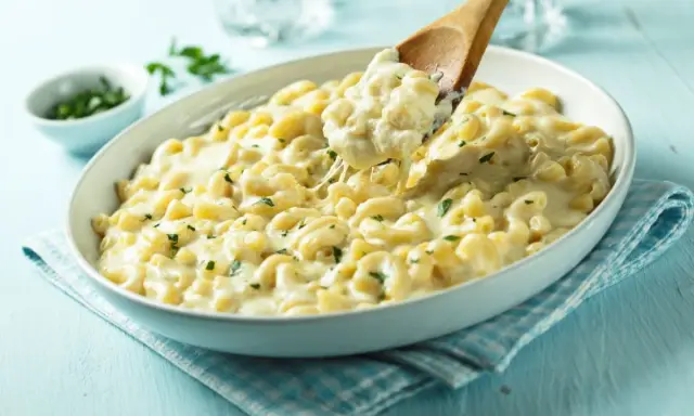 Pyszne mac and cheese przepis w białej misce, z drewnianą łyżką nabierającą porcję kremowego makaronu z serem.