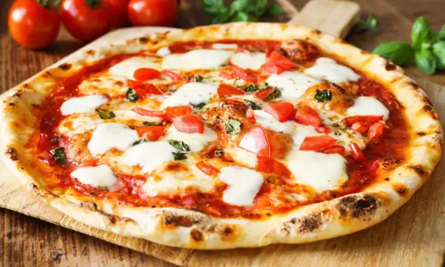 Pyszne ciasto na pizzę bez wyrastania, z pomidorami i mozzarellą, na drewnianej desce.