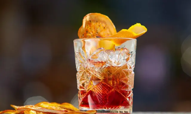 Klasyczny whisky old fashioned w kryształowej szklance, ozdobiony skórką pomarańczy i suszonym owocem.