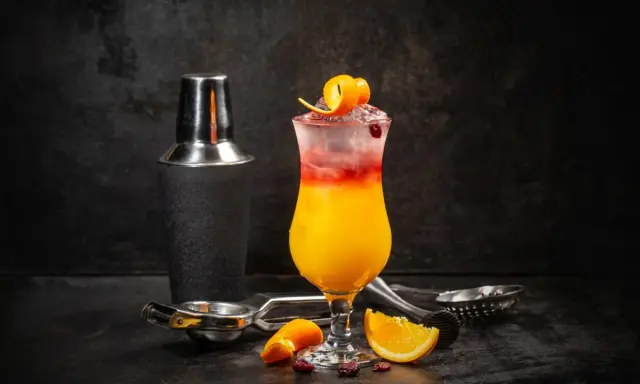 Kolorowy drink Sex on the Beach z pomarańczą i żurawiną, obok shakera i akcesoriów barmańskich. Idealny przepis na lato!