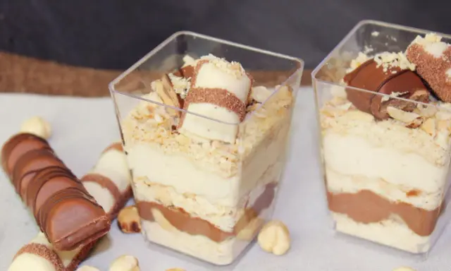 Pyszne ciasto Kinder Bueno w pucharkach, przełożone kremem i czekoladą, posypane orzechami.
