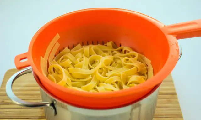 Ugotowany makaron w pomarańczowym durszlaku. Zastanawiasz się, czy można zamrozić ugotowany makaron? Tak, jest to możliwe!