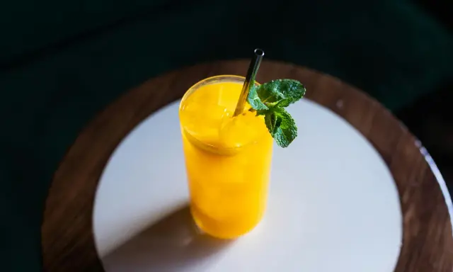 Orzeźwiający drink z mango, z kostkami lodu i listkiem mięty, podany w szklance ze słomką.