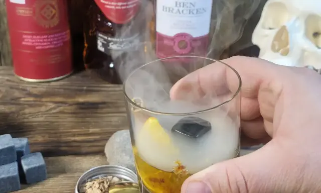 Szklanka z drinkiem otoczona dymem, obok butelki whisky i czaszka. Wyjątkowe drinki z dymem.