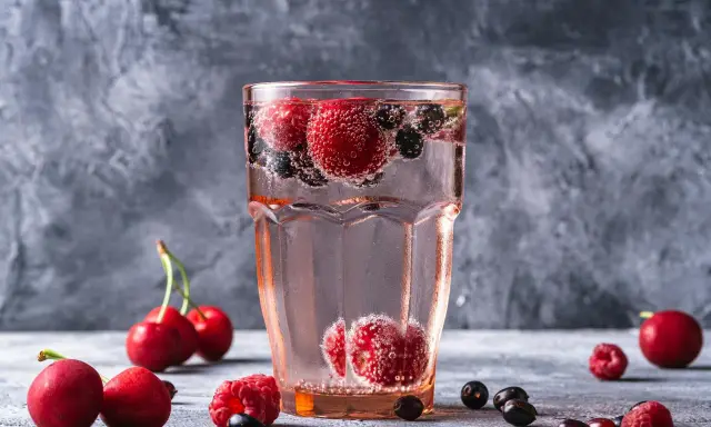 Orzeźwiający drink z wódką malinową, pełen malin, wiśni i borówek, bąbelkuje w szklance.