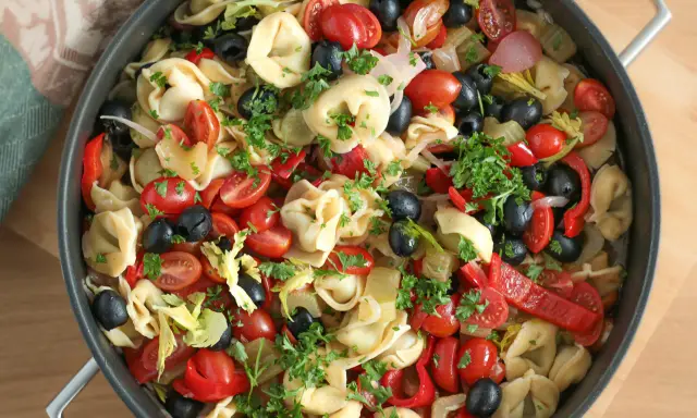 Kolorowa sałatka z tortellini, pomidorkami koktajlowymi, czarnymi oliwkami, papryką i natką pietruszki w dużej patelni.