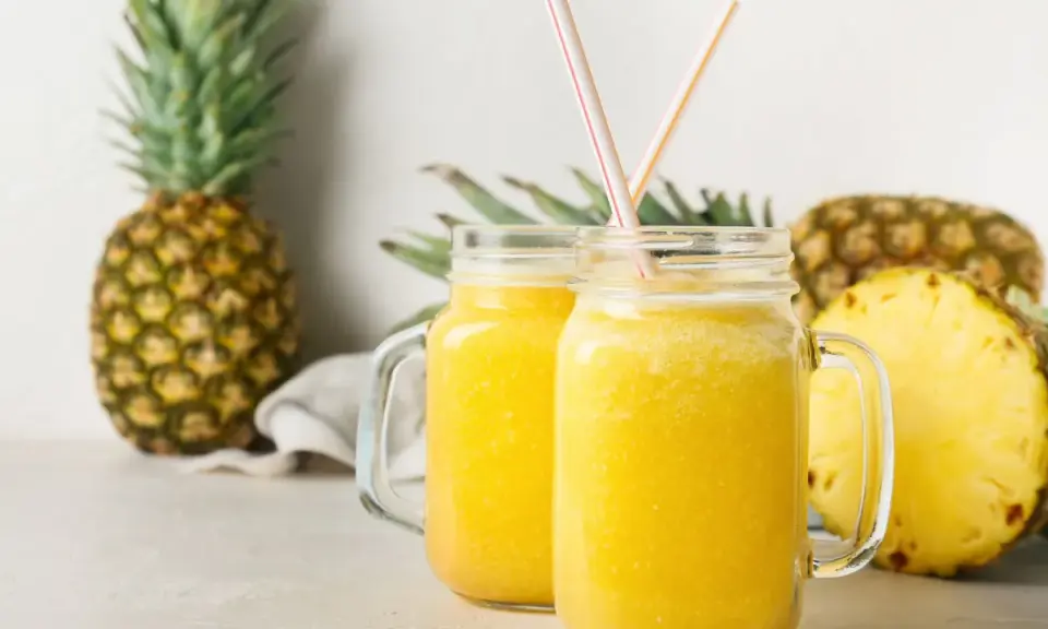 Orzeźwiający drink w ananasie, podany w słoikach, z kawałkami ananasa w tle.