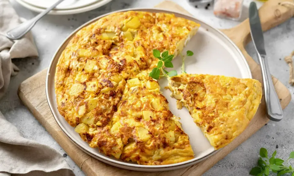 Złocista frittata z ziemniakami, pokrojona na kawałki, podana na talerzu z gałązką ziół.