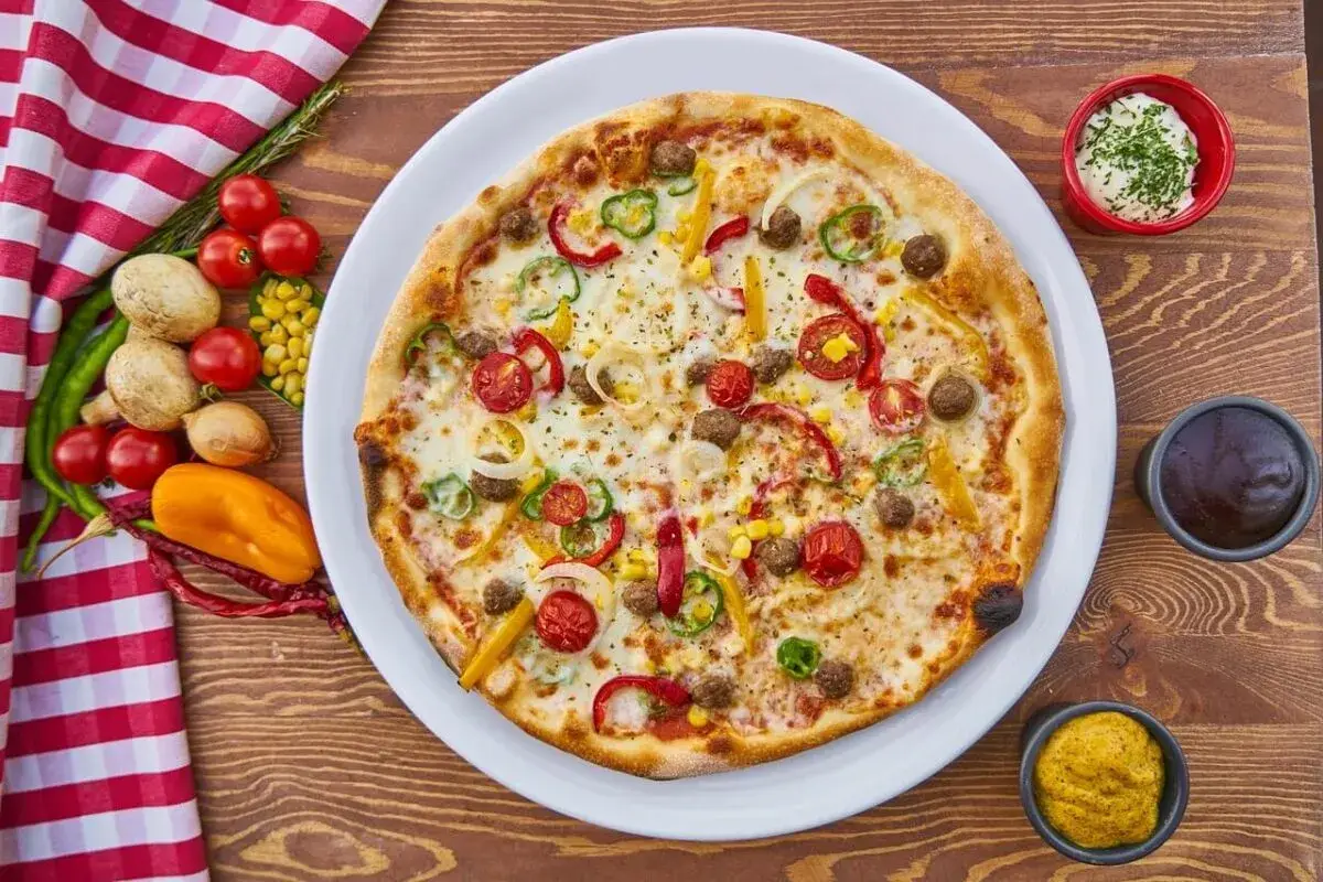 Pizza z mięsem mielonym, papryką, cebulą i kukurydzą. Obok sosy i warzywa, co zamiast śmietany?