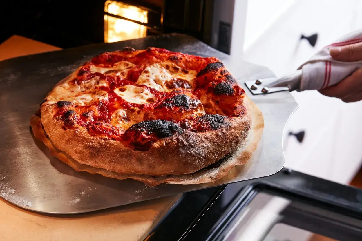 Gorąca, świeżo upieczona pizza z ciągnącym się serem i lekko przypalonymi brzegami jest wyjmowana z piekarnika.