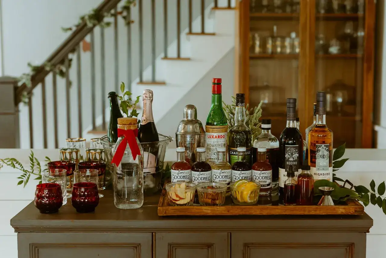 Elegancki drink bar DIY z butelkami ginu, likierów, szampanem i akcesoriami. Idealny na domowe przyjęcie.