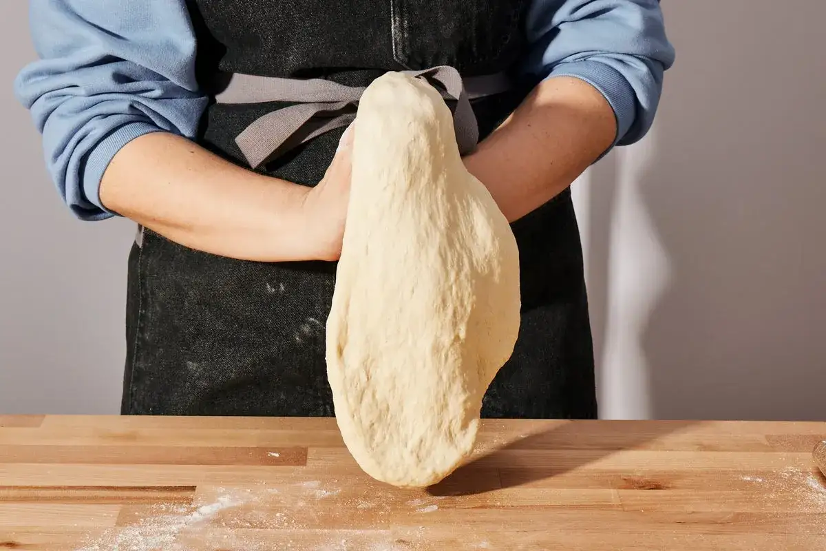 Ręce formują ciasto na pizzę. Czy ciasto na pizzę można zrobić dzień wcześniej? Tak, to świetny sposób na oszczędność czasu.