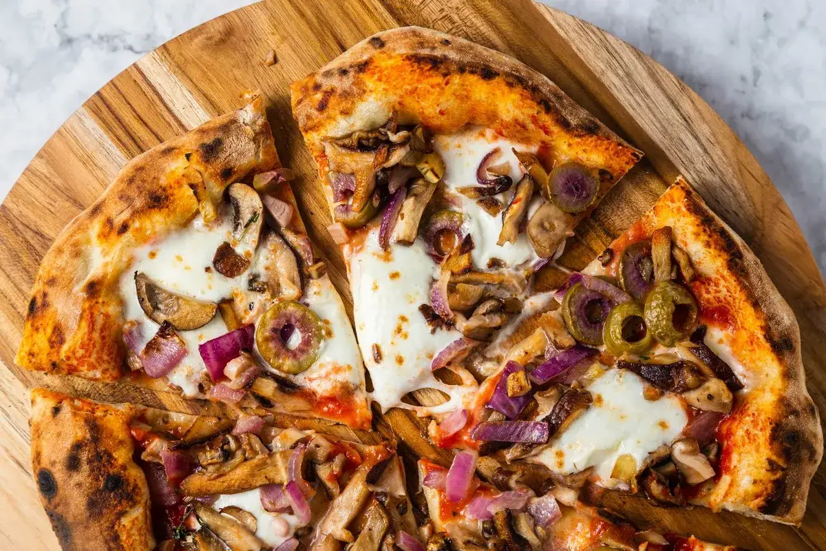 Pyszna pizza z pieczarkami do pizzy, cebulą i oliwkami na drewnianej desce.