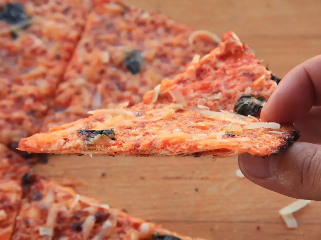 Chrupiący kawałek pizzy z tortilli, z pomidorowym sosem i serem, podniesiony do ust.